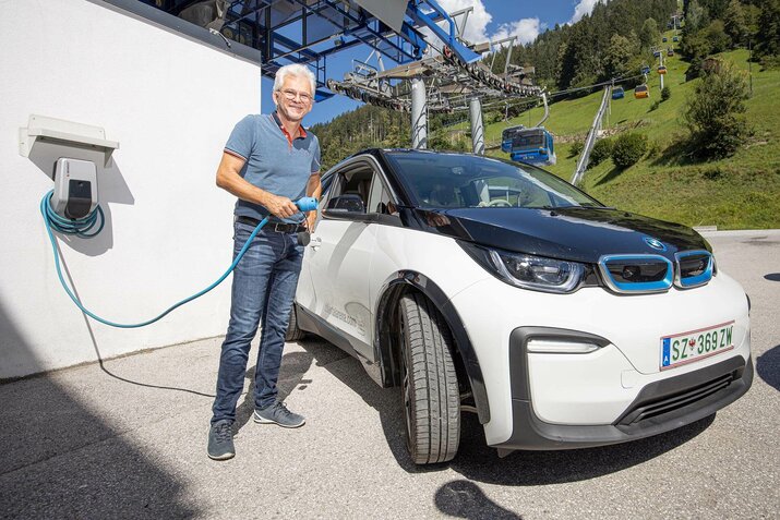 Ein Mann steht vor einem E-Auto und hält das Ladekabel in der Hand