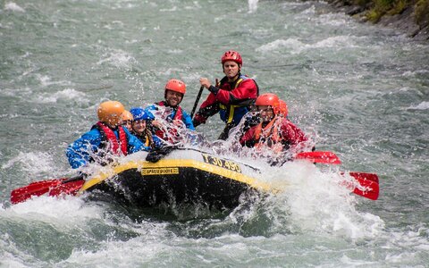 Sechs Personen in Sicherheitsausrüstung beim Wildwasser-Rafting.