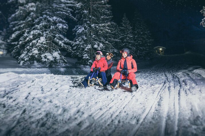 Ein Mann und zwei Frauen fahren auf ihren Rodeln die Strecke hinunter