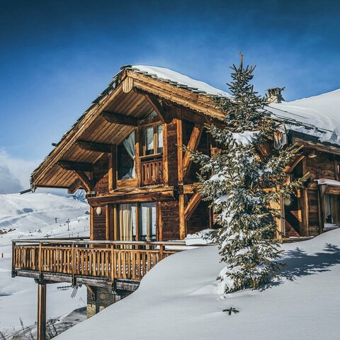 Holzhaus, das von Schnee bedeckt ist, mit winterlicher Atmosphäre und verschneiten Bäumen rundherum