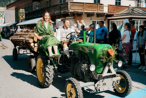 Ein Mann und eine Frau fahren auf einem grünen Traktor durch den Bauernmarkt.