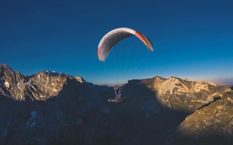Ein Paragleiter fliegt über eine Berglandschaft.