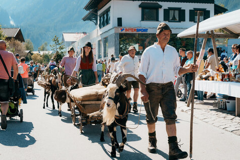 Personen in Trachtenkleidung führen Ziegen durch den Bauernmarkt.