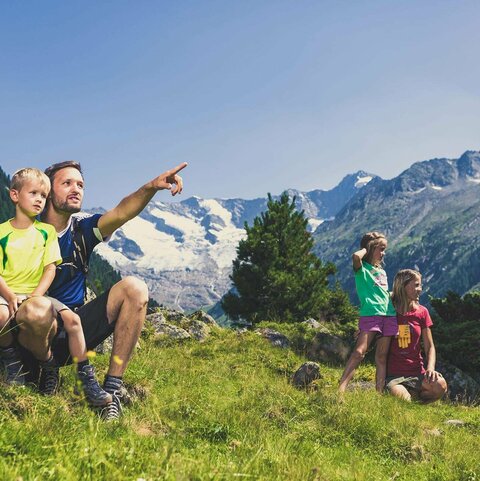 Eine Familie sitzt auf einer Wiese und blickt auf eine traumhafte Bergkulisse