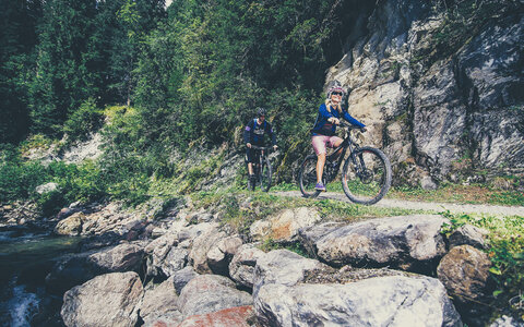 Zwei Radfahrer radeln an einem Fluss entlang.