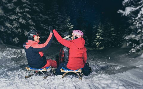 Ein Mann und zwei Frauen sausen auf ihren Rodeln die Strecke hinunter