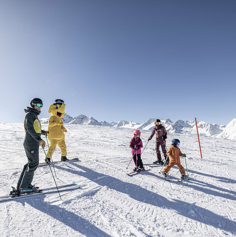 Eine Familie auf Skiern steht mit dem Maskottchen Funty auf der Piste