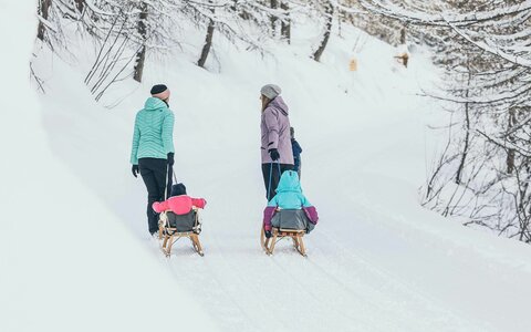 Zwei Frauen ziehen ihre Kinder durch den Schnee auf Rodeln