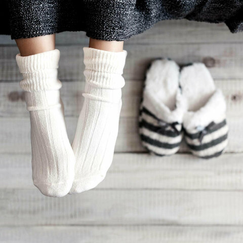 Zwei Füße mit weißen Socken neben zwei Hausschuhen.