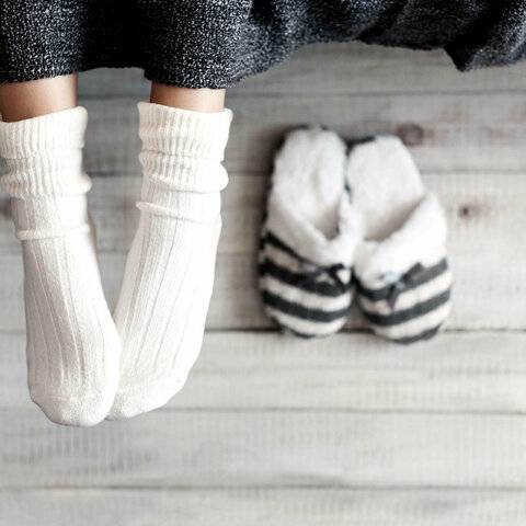 Zwei Füße mit weißen Socken neben zwei Hausschuhen.