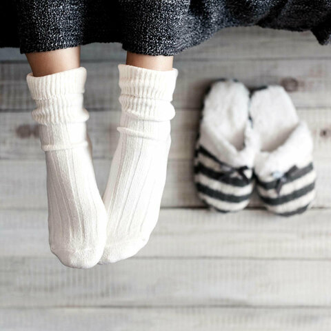 Zwei Füße mit weißen Socken neben zwei Hausschuhen.