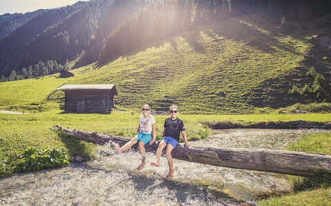 Zwei Kinder sitzen auf einem Holzstamm und plantschen im Wasser