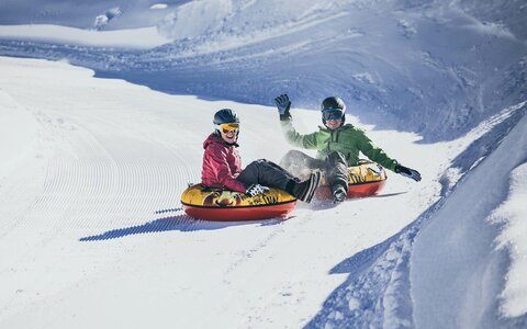Zwei Personen fahren auf luftgefüllten Reifen die Piste hinunter