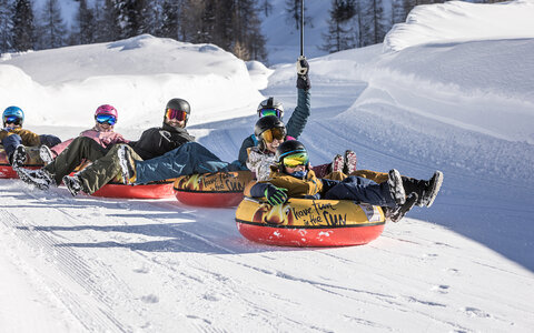 Eine Familie fährt auf Reifen die Piste hinunter