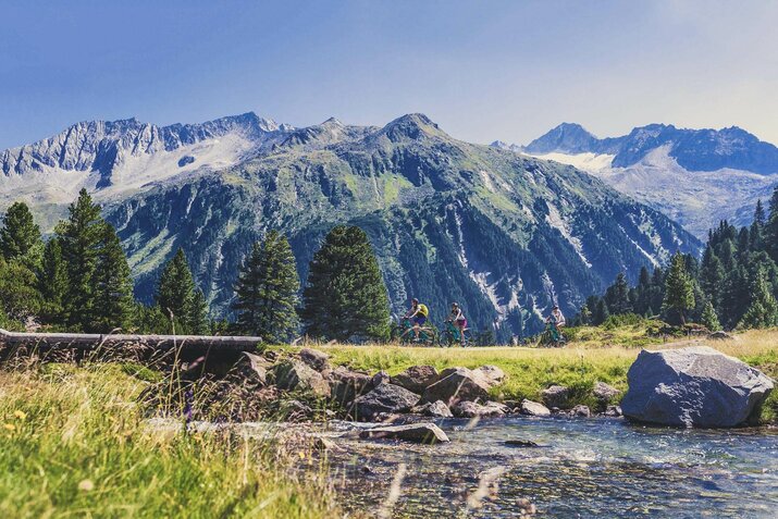 Drei Radfahrer radeln durch die Landschaft, mit traumhafter Bergkulisse im Hintergrund.
