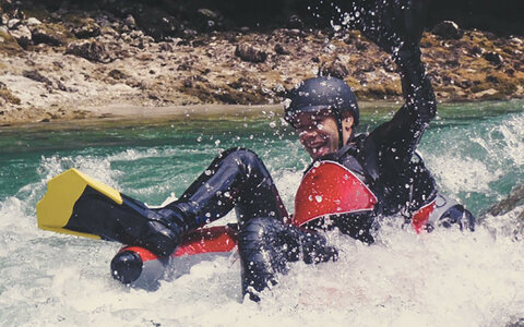 Eine Person treibt mit Helm und Flossen in roten Reifen durch sprudelndes Wildwasser.