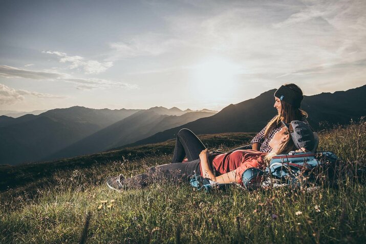 Zwei Frauen liegen in einer Wiese und blicken auf eine traumhafte Bergkulisse