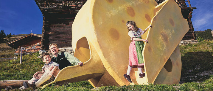 Ein Mann und zwei Kinder spielen bei einer großen Käsestatue