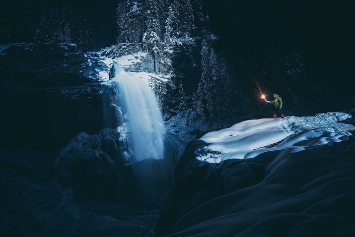 Ein Mann steht mit einer Fackel neben einem Wasserfall