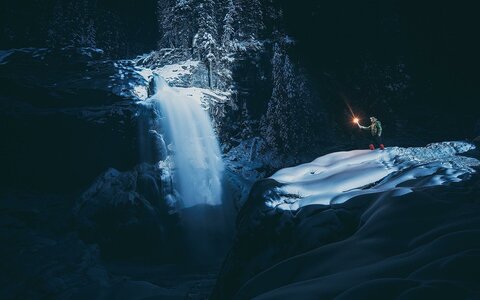 Ein Mann steht mit einer Fackel neben einem Wasserfall