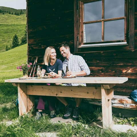 Ein Mann und eine Frau essen eine Brotjause bei einer Hütte
