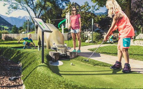 Eine Frau und zwei Kinder spielen Minigolf
