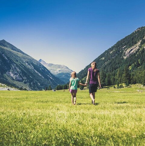 Eine Frau und ein Mädchen gehen händchenhaltend über eine Wiese 