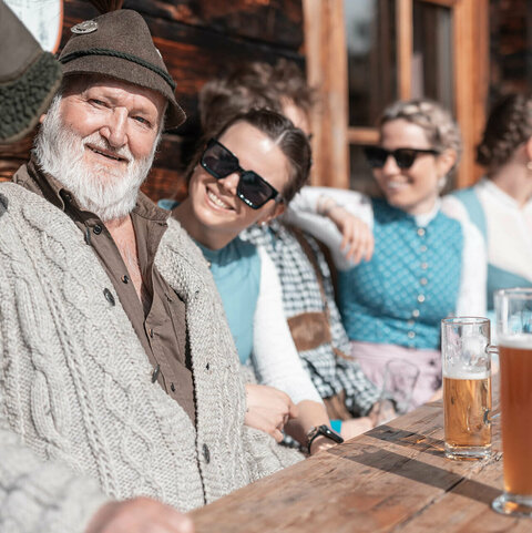 Männer und Frauen in Trachtenkleidung sitzen bei einer Hütte