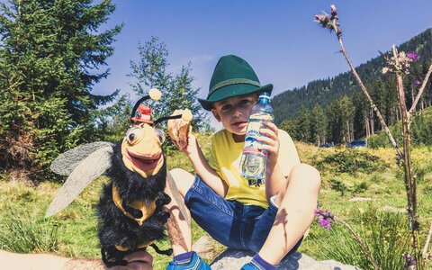 Ein Junge sitzt mit einem Wurstsemmel und einer Wasserflasche auf einem Stein