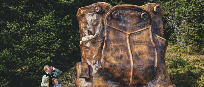 Ein Mädchen sitz in einer großen Lederhosenstatue