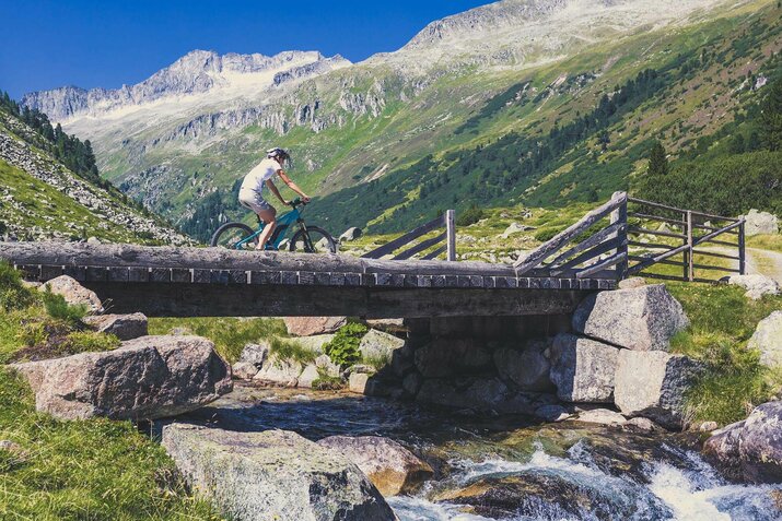 Eine Radfahrerin fährt über eine kleine Holzbrücke.