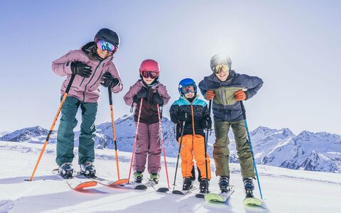 Eine Frau, ein Mann und zwei Kinder stehen auf der Piste auf ihren Skiern