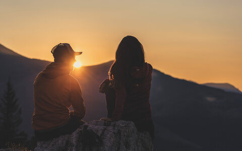 Ein Mann und eine Frau sitzen auf einem Stein und beobachten den Sonnenaufgang