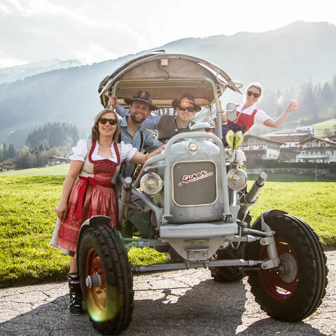 Zwei Männer und zwei Frauen in Trachtenkleidung sitzen auf einem Traktor
