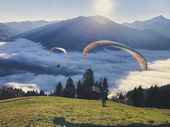 Paragleiter fliegen über einer Wolkendecke bei Sonnenaufgang.