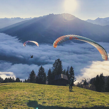 Paragleiter fliegen über einer Wolkendecke bei Sonnenaufgang.