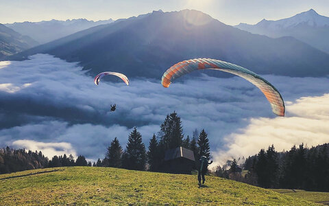 Paragleiter fliegen über einer Wolkendecke bei Sonnenaufgang.