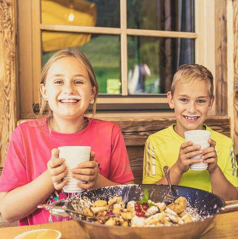 Ein Junge und ein Mädchen sitzen vor einem Kaiserschmarrn und trinken ein Glas Milch