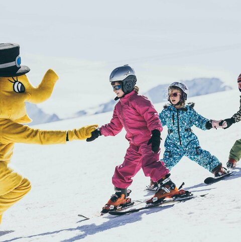 Drei Kinder auf Skiern mit dem Maskottchen Funty