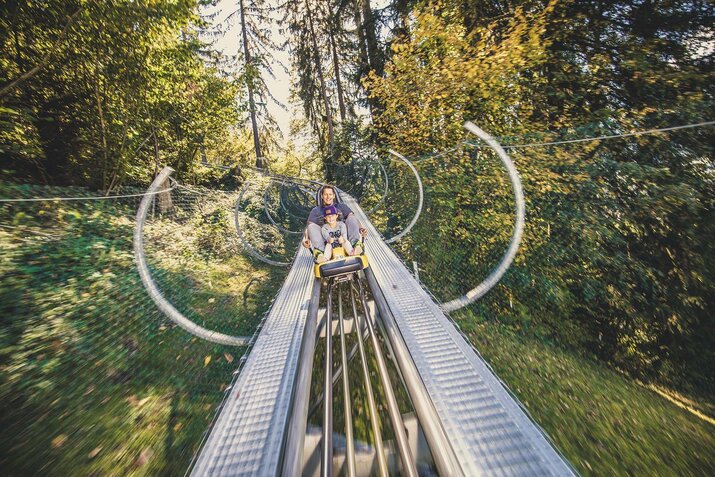 Ein Mann und ein Mädchen fahren mit einer Sommerrodelbahn.