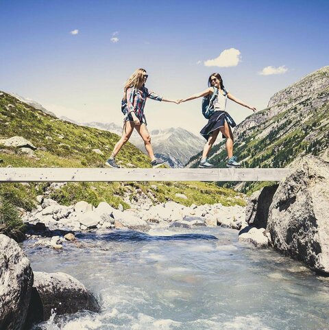 Zwei Frauen gehen händchenhaltend über eine Holzbrücke