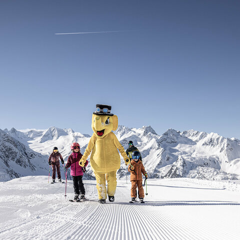 Hand in Hand mit dem Maskottchen Funty gehen zwei Kinder über die Piste