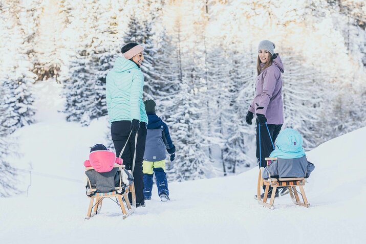 Zwei Frauen ziehen ihre Kinder durch den Schnee auf Rodeln